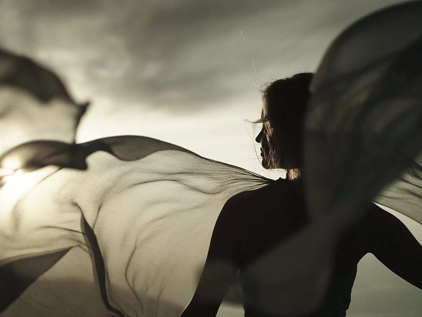 Young woman in long summer dress flying in the wind standing on a rocky shore